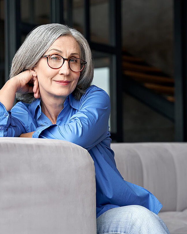 Frau mit Brille auf einer Couch mit Blick in die Kamera